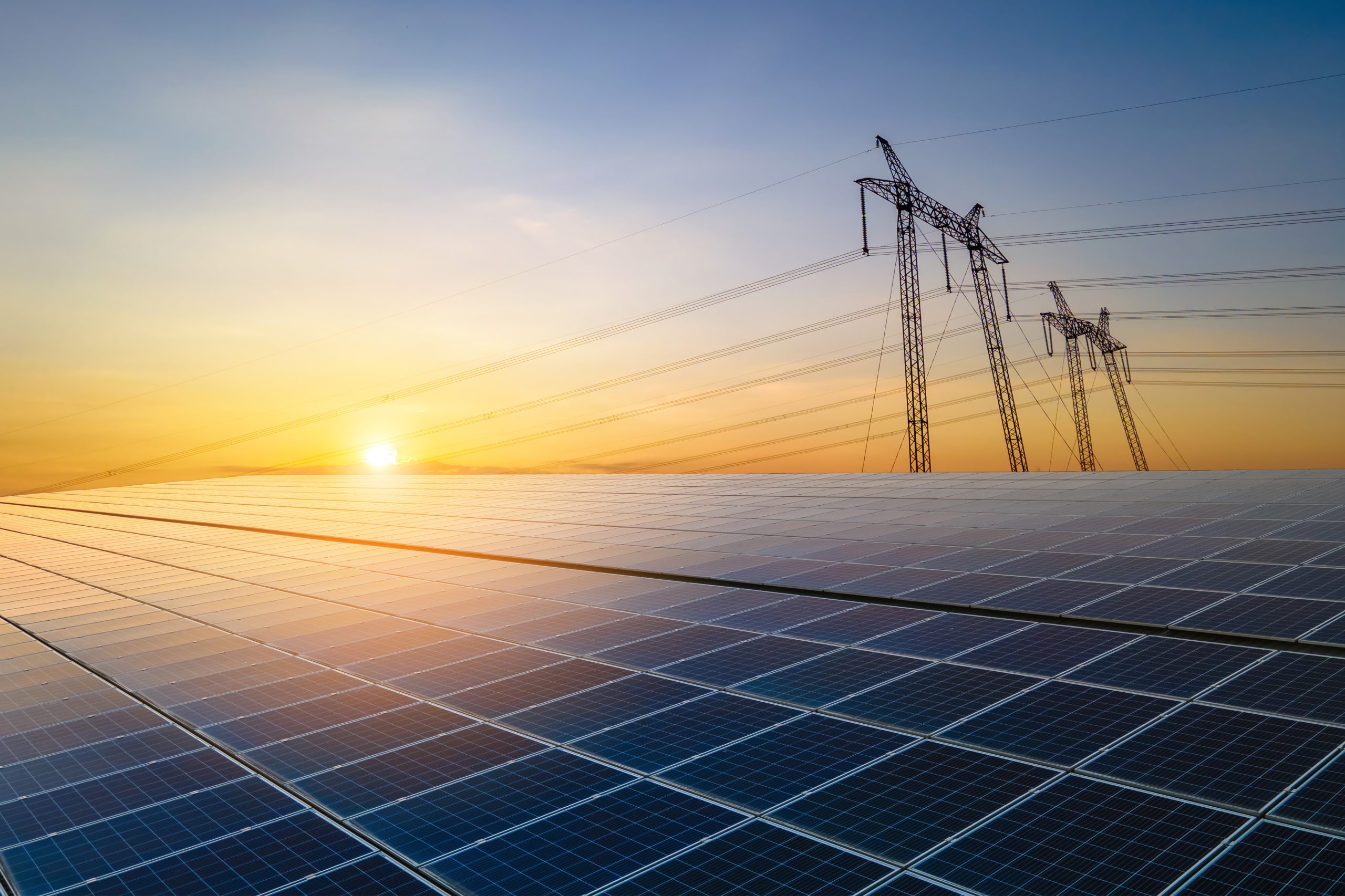High voltage pylons with electric power lines transfering electricity from solar photovoltaic sells at sunrise. Production of sustainable energy concept.